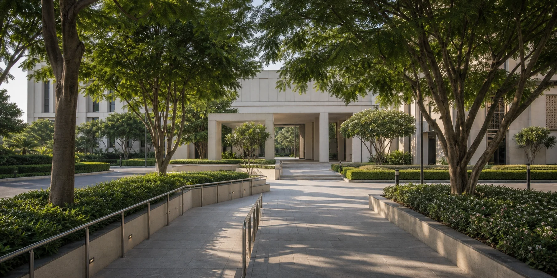 Institutional forecourt landscape with mature trees, lawn, and formal pedestrian arrival routes.