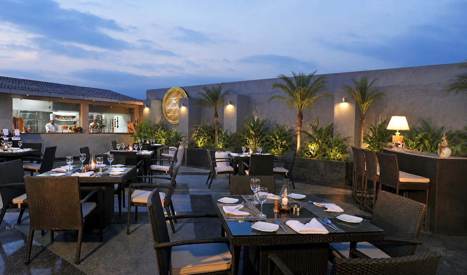 Open-air restaurant terrace at Country Inn Gurugram with perimeter palms, structured planters and evening dining tables.