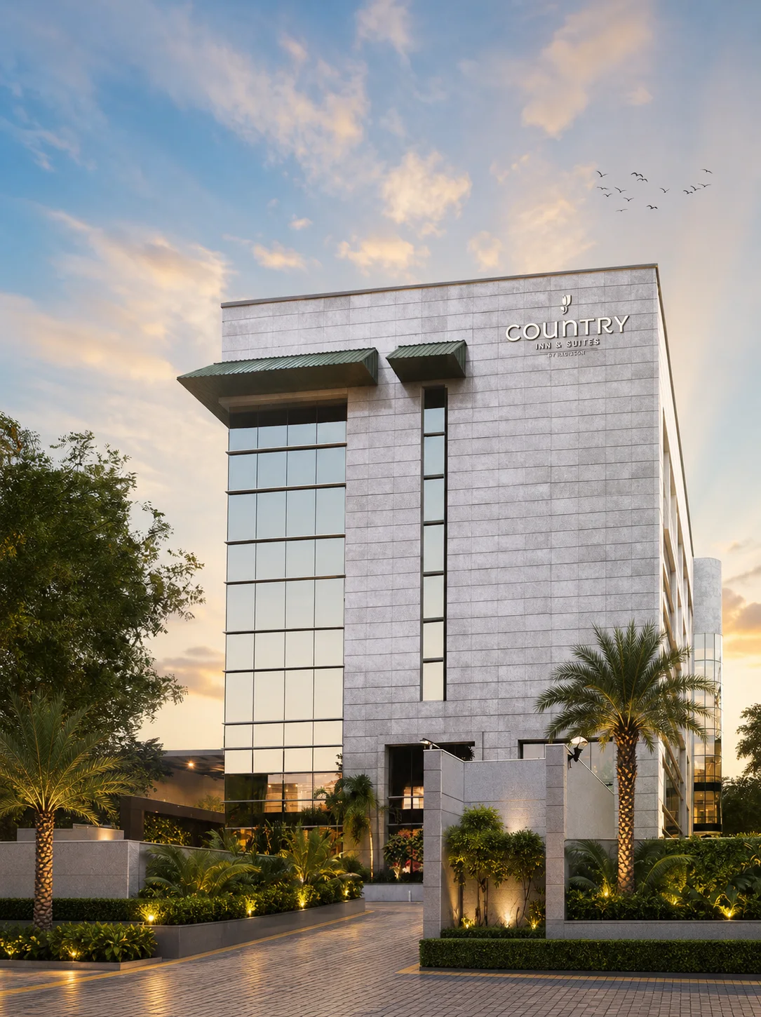 Country Inn & Suites Gurugram hotel facade and arrival court framed by palms, low planting and an illuminated entrance.