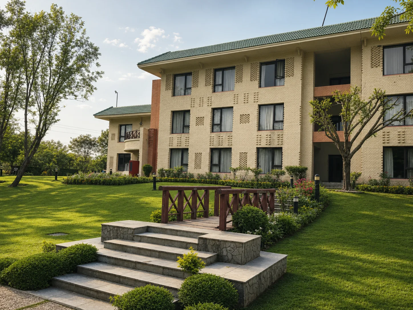 Country Inn Jammu garden wing with lawn, timber footbridge, stone steps, mature trees and structured border planting.
