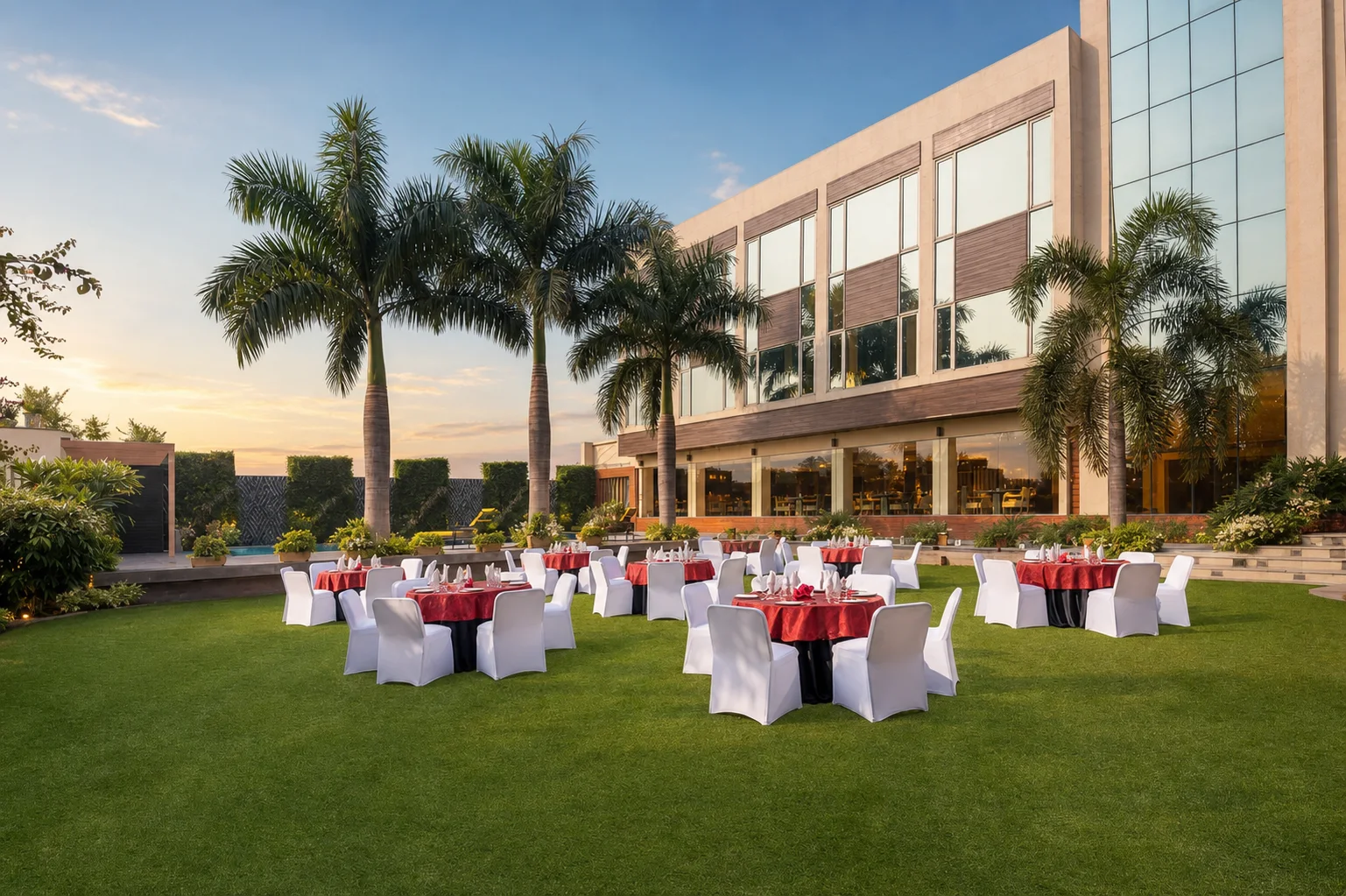 Country Inn Jammu event lawn with banquet tables, mature palms, structured perimeter landscape and the hotel facade at golden hour.