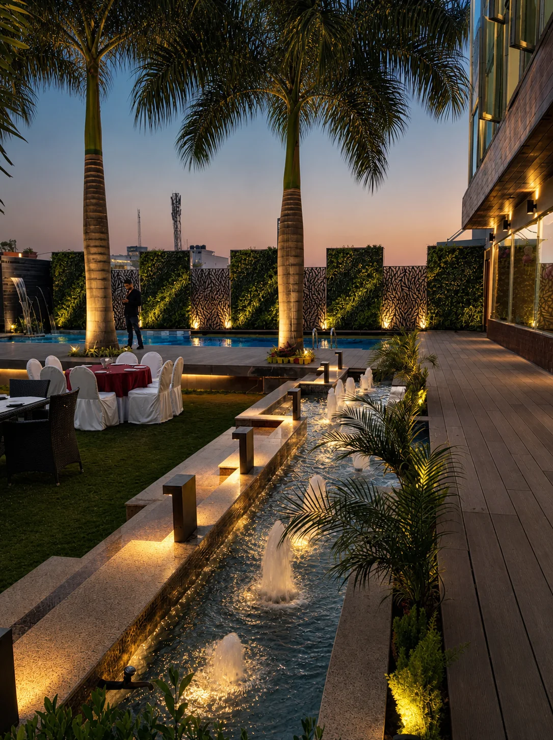 Country Inn Jammu poolside event garden with illuminated fountain jets, palms, planted walls and warm architectural lighting.