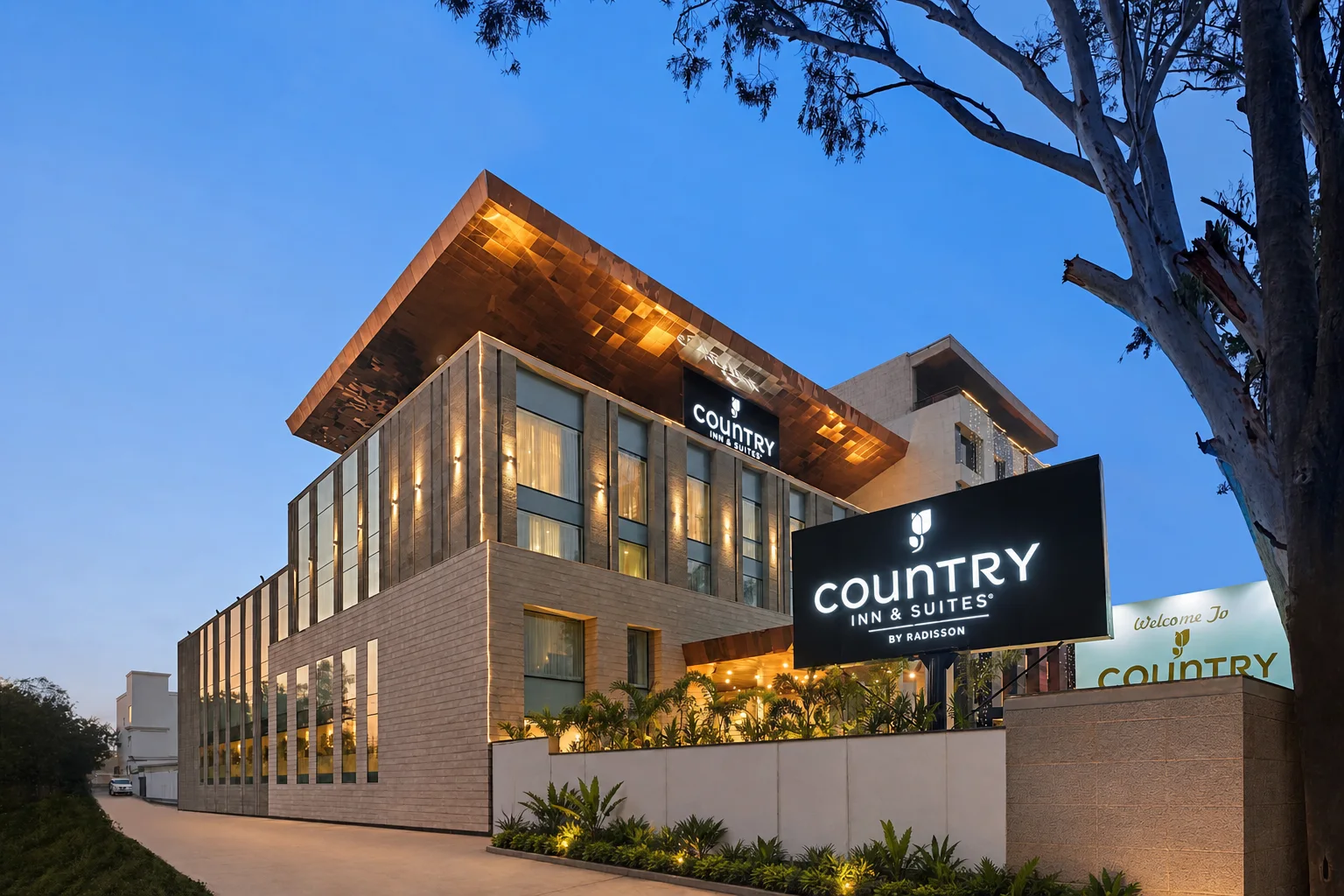 Country Inn & Suites Zirakpur exterior at blue hour with an illuminated canopy and arrival planting