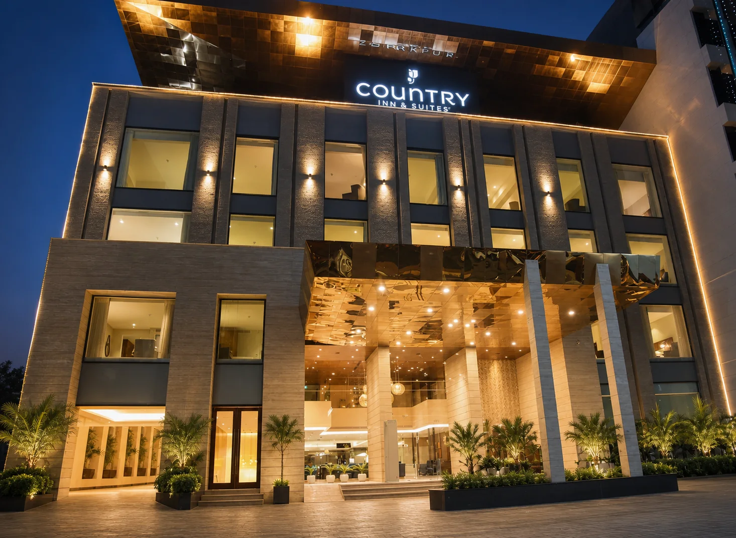 Country Inn & Suites Zirakpur entrance facade at blue hour with warm lighting, polished arrival paving and structured palms.