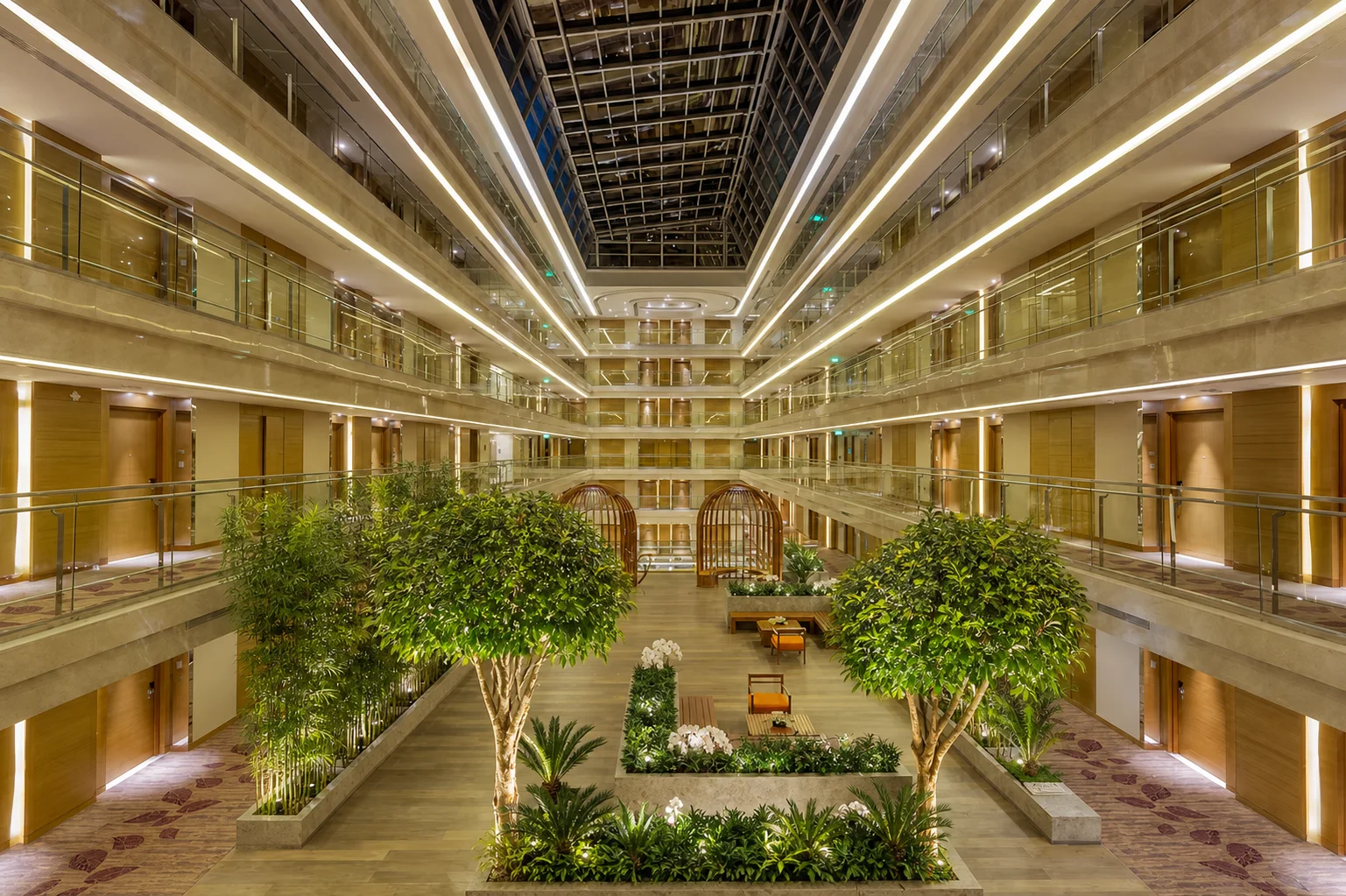 Holiday Inn Jaipur atrium with pruned feature trees, layered tropical foliage and white orchids beneath guest-room galleries.