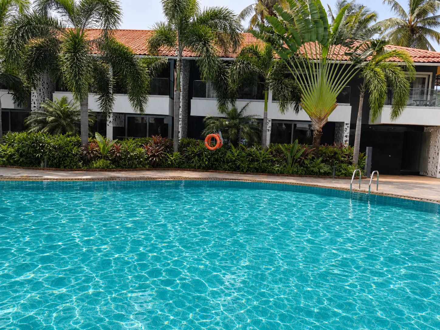 Hyatt Place Goa Candolim daytime pool beneath foxtail and traveller palms beside the guest-room facade
