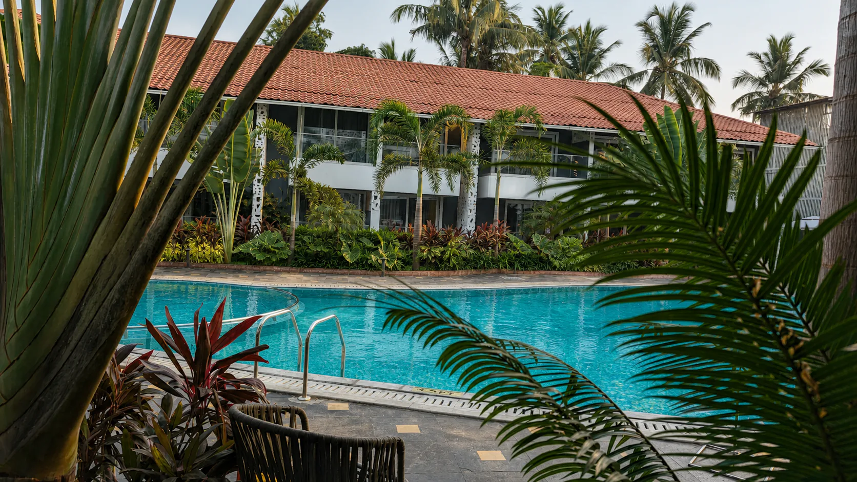 Hyatt Place Goa Candolim pool and guest-room facade framed by traveller and areca palm foliage