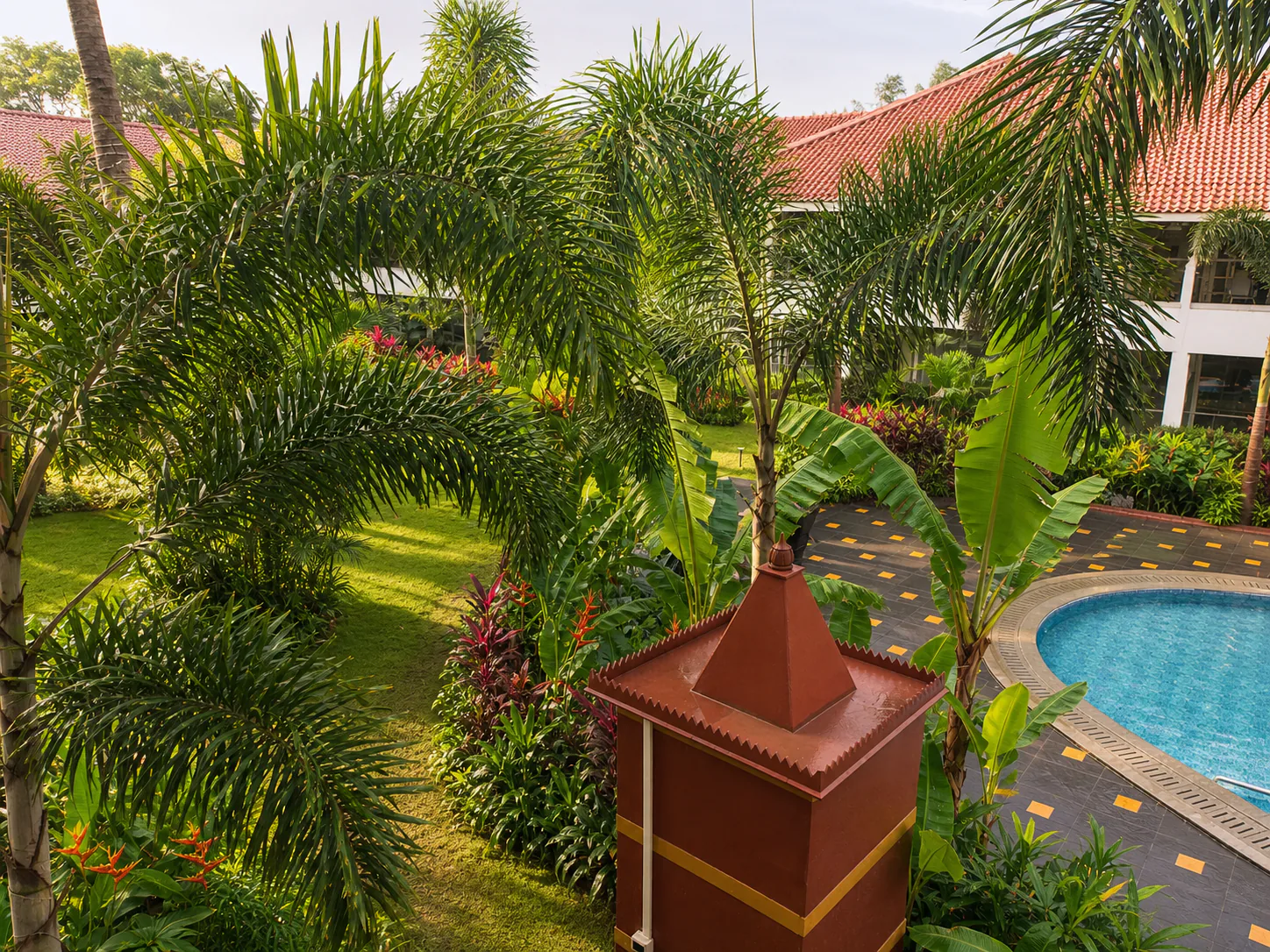 Hyatt Place Goa Candolim elevated garden with red pavilion feature, foxtail palms, lawn and resort pool