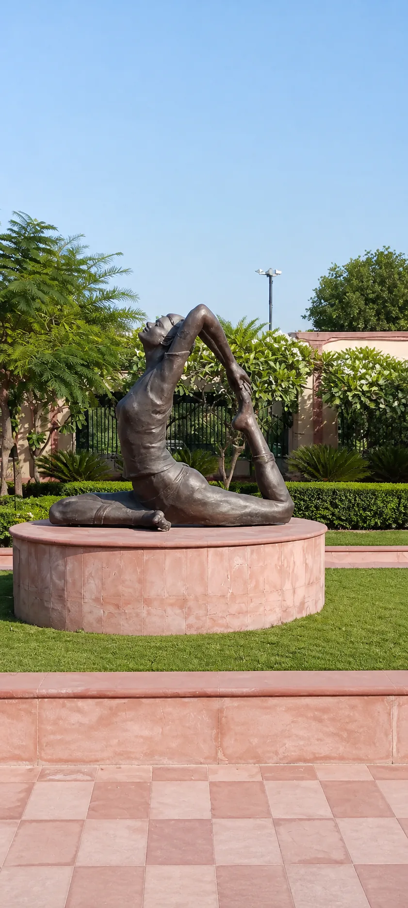 Made Easy School Bhandwari bronze yoga sculpture on a sandstone pedestal surrounded by lawn, hedges, cycads and plumeria