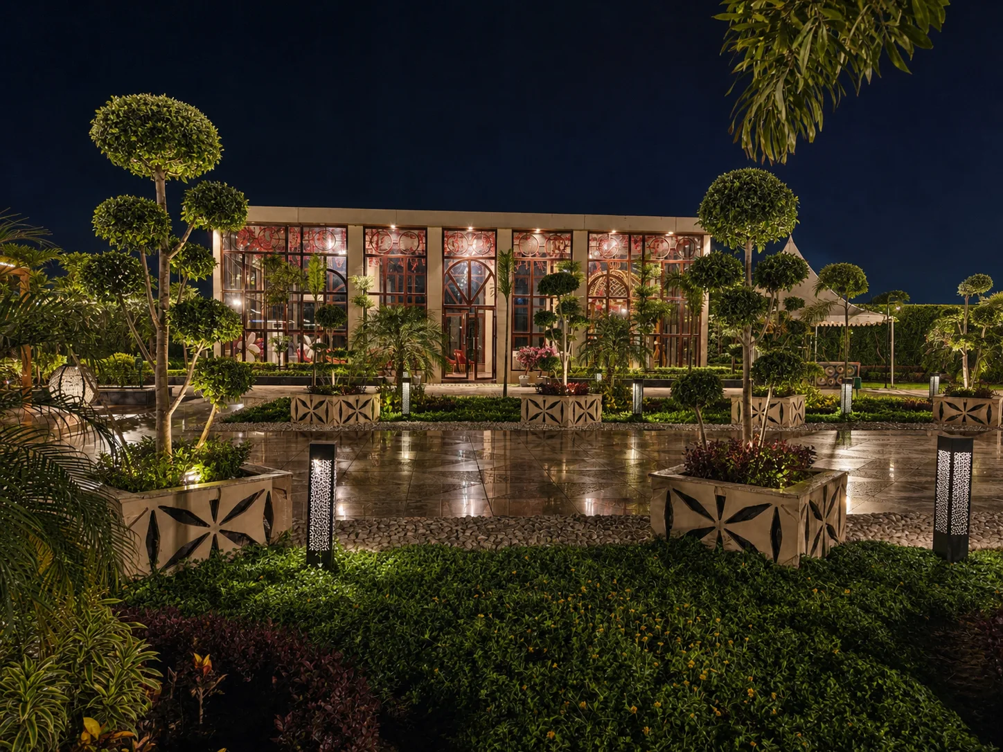 One Farrer illuminated glass pavilion framed by sculptural topiary, layered garden beds and restrained bollard lighting.
