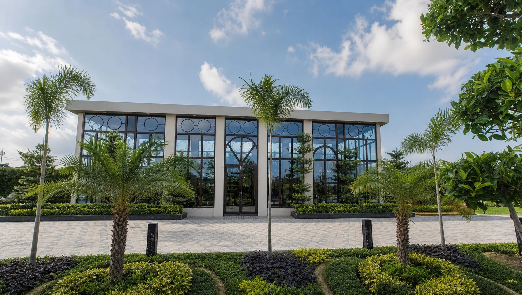 One Farrer glass pavilion in daylight with healthy palms, layered beds, lawn and clean reflective glazing.