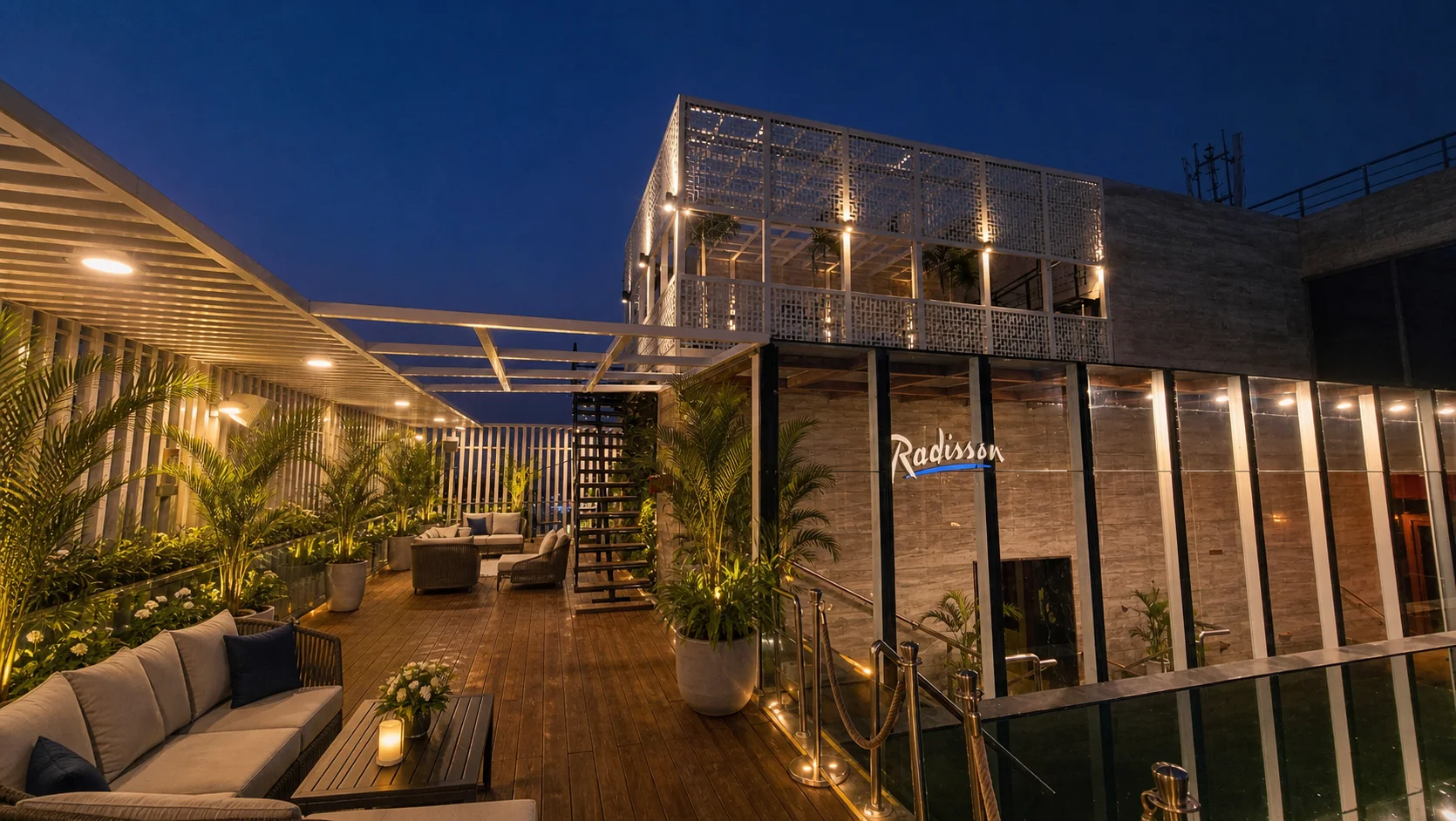 Radisson Lucknow rooftop lounge with coordinated palms, evergreen foliage, white flowers and warm architectural lighting.