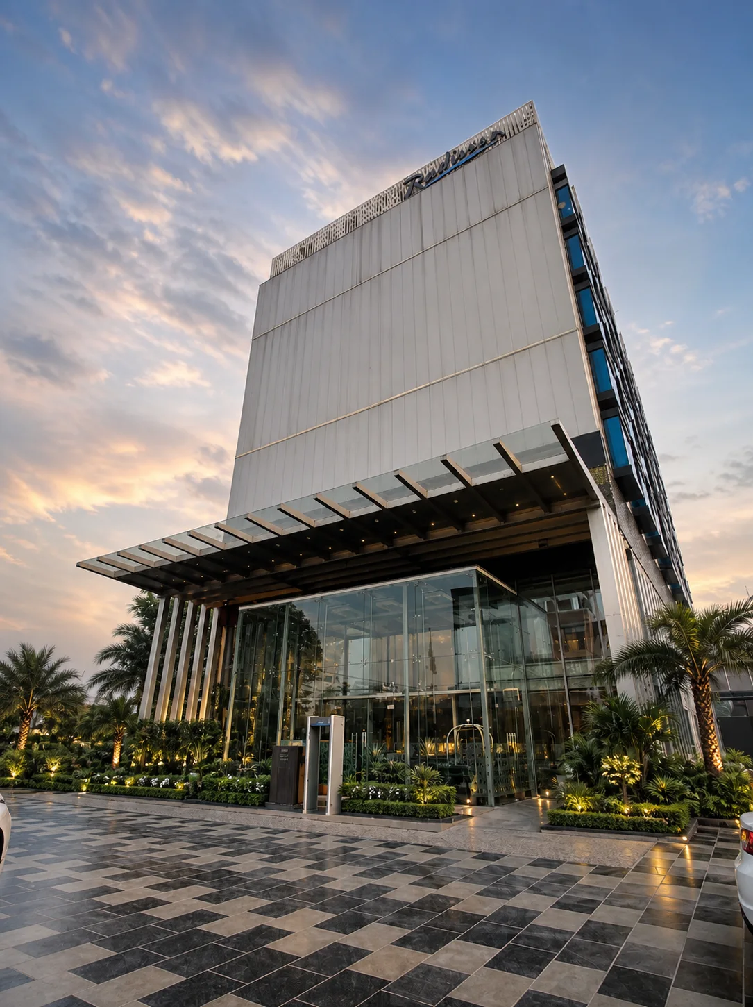 Radisson Lucknow tower and glass entrance framed by sculptural palms, clipped hedges and golden-hour lighting.