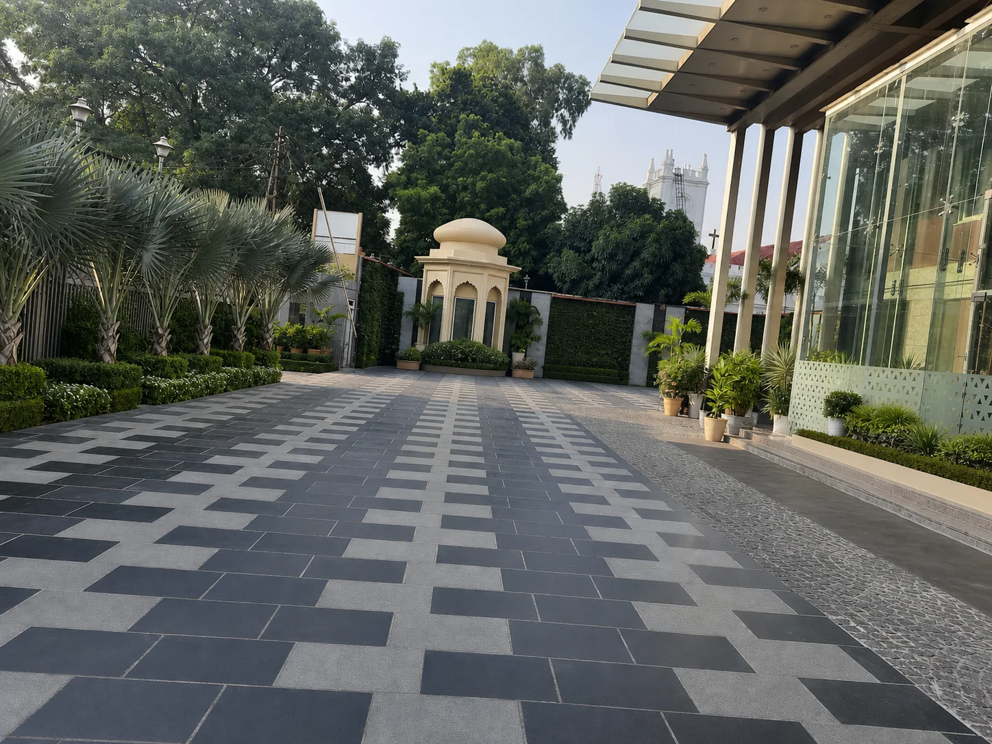 Radisson Lucknow arrival courtyard with geometric paving, structured palms, hedges and restrained white flowering accents.