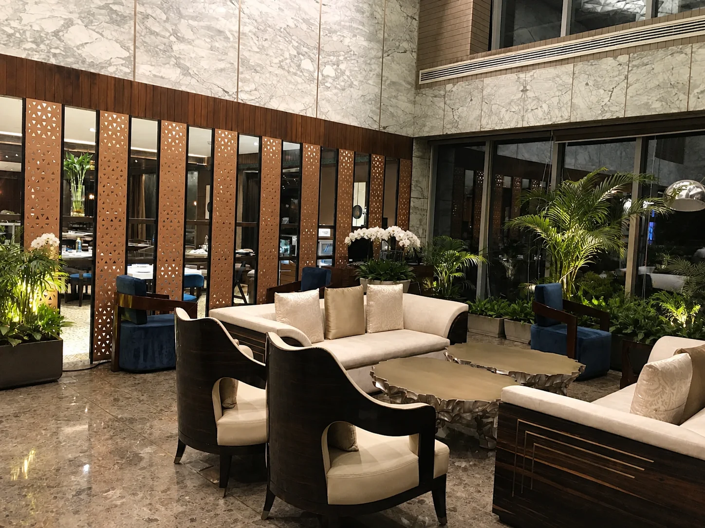Radisson Lucknow marble hotel lounge with coordinated tropical planters, compact palms and white orchids.