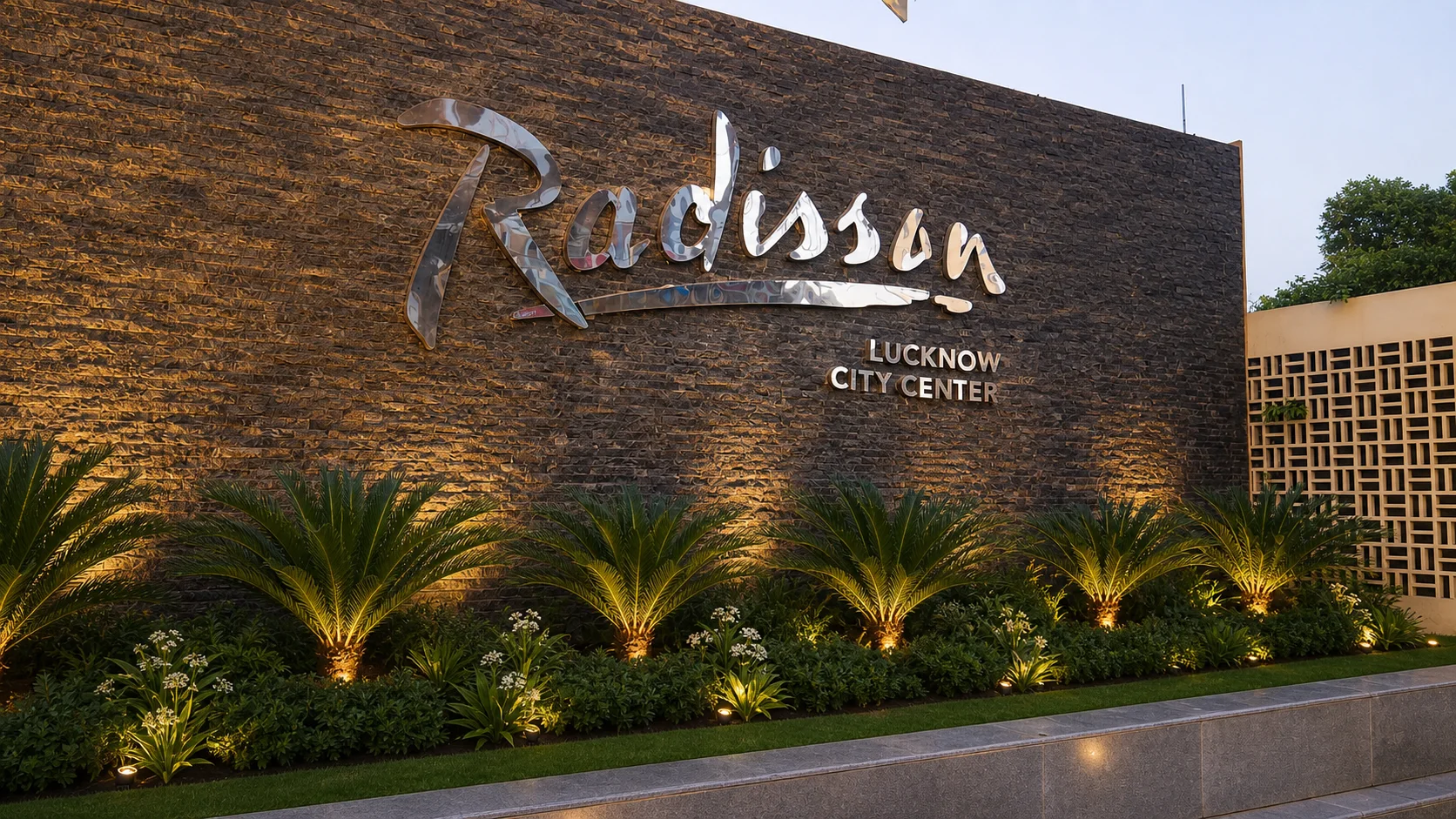 Radisson Lucknow identity wall with illuminated cycads, evergreen groundcover and white flowering accents.