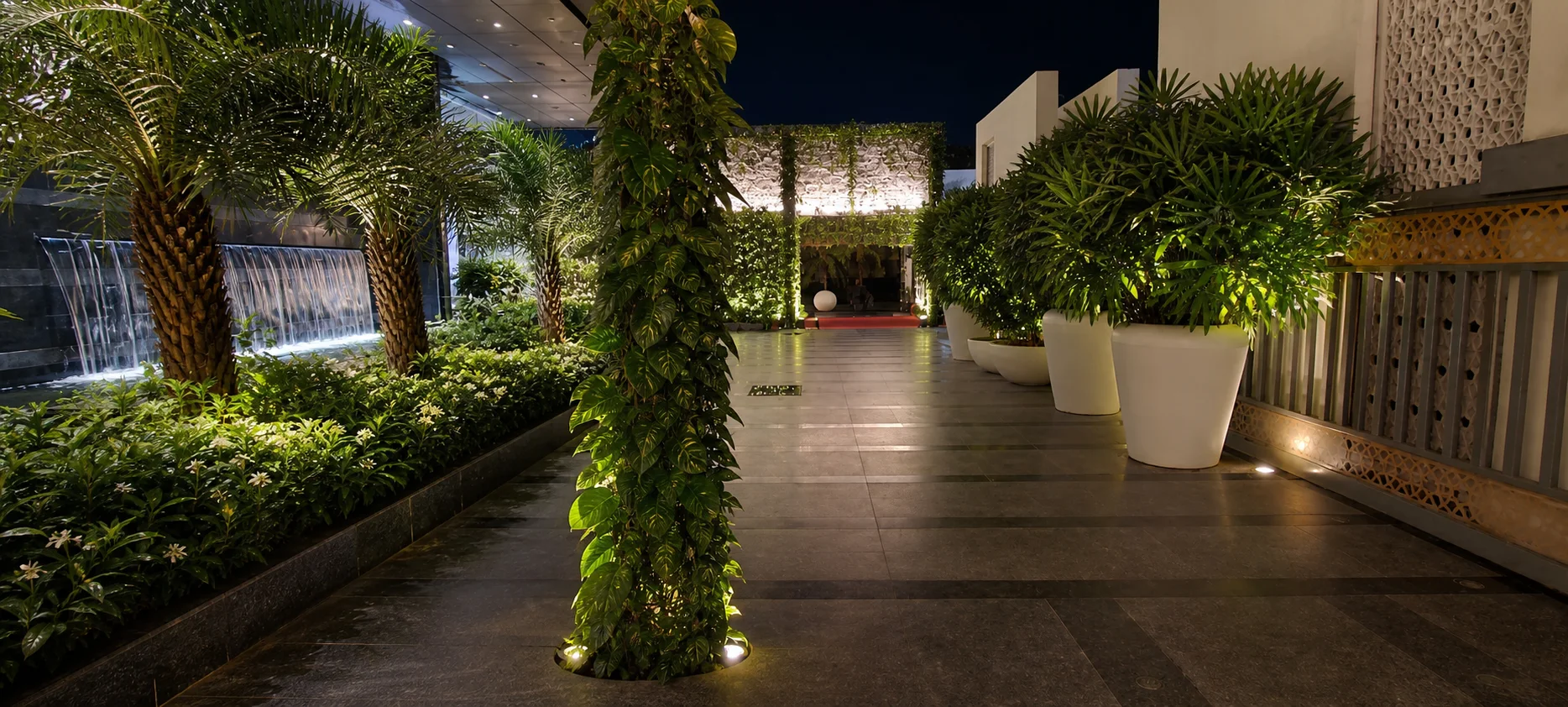 Silver Spoons illuminated garden passage with palms, a planted column, waterfall and coordinated tropical planters.