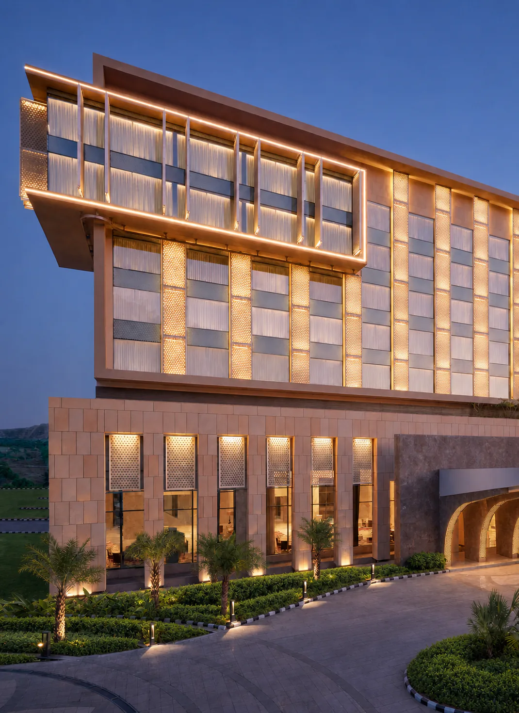 Taj Amer Jaipur arrival facade at dusk with palms, geometric planting beds and warm architectural lighting.