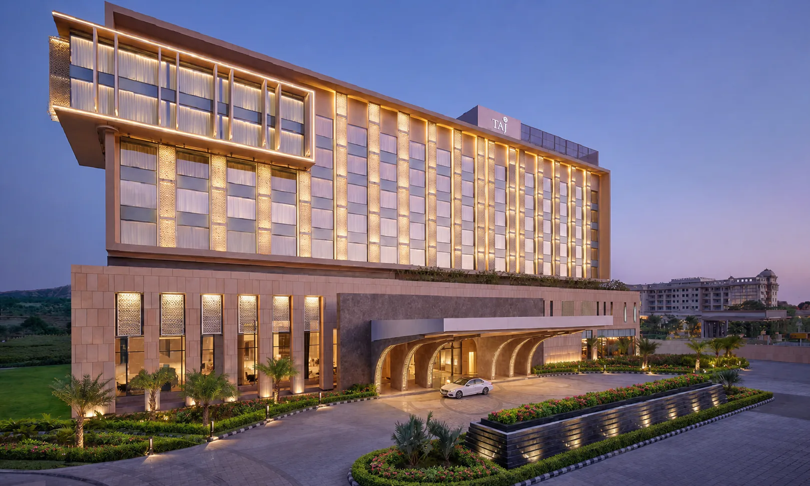 Taj Amer Jaipur five-star hotel entrance with stone paving, layered tropical planting and landscape lighting
