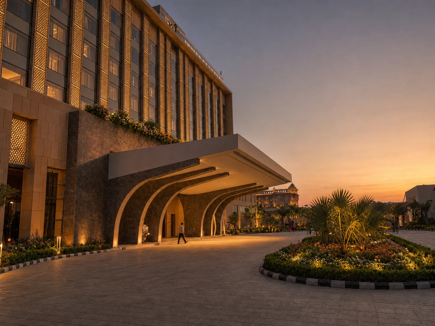 Taj Amer Jaipur porte-cochere at evening with warm facade lighting and a circular palm-and-flower arrival island.