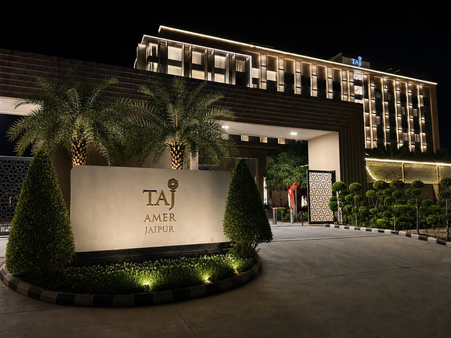 Taj Amer Jaipur outer gate at night with the illuminated hotel sign, structured palms and restrained landscape lighting.