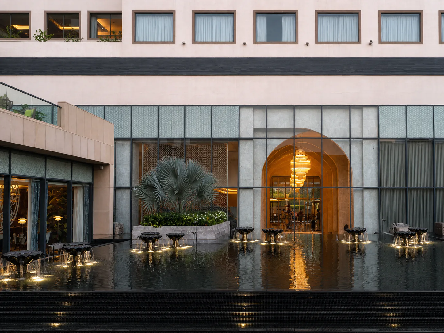 Straight-on view of the Taj Amer Jaipur lobby courtyard with cascading lotus bowls, underwater lights and a reflective pool.