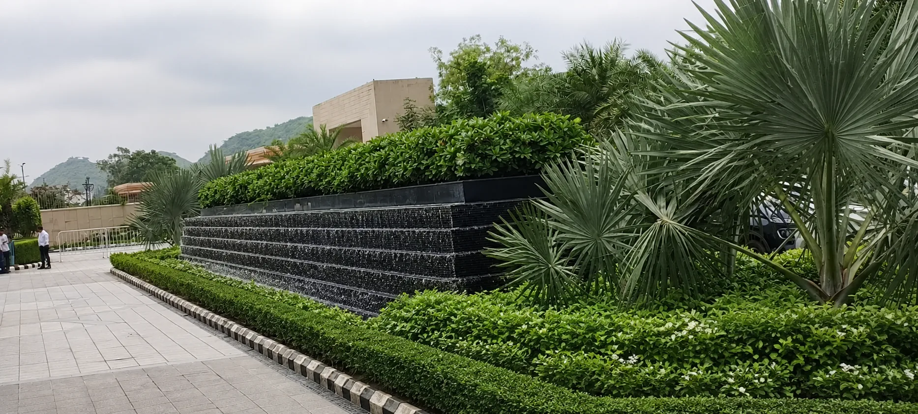 Long black water wall at the Taj Amer Jaipur arrival with a continuous cascade, silver fan palms and clipped planting.