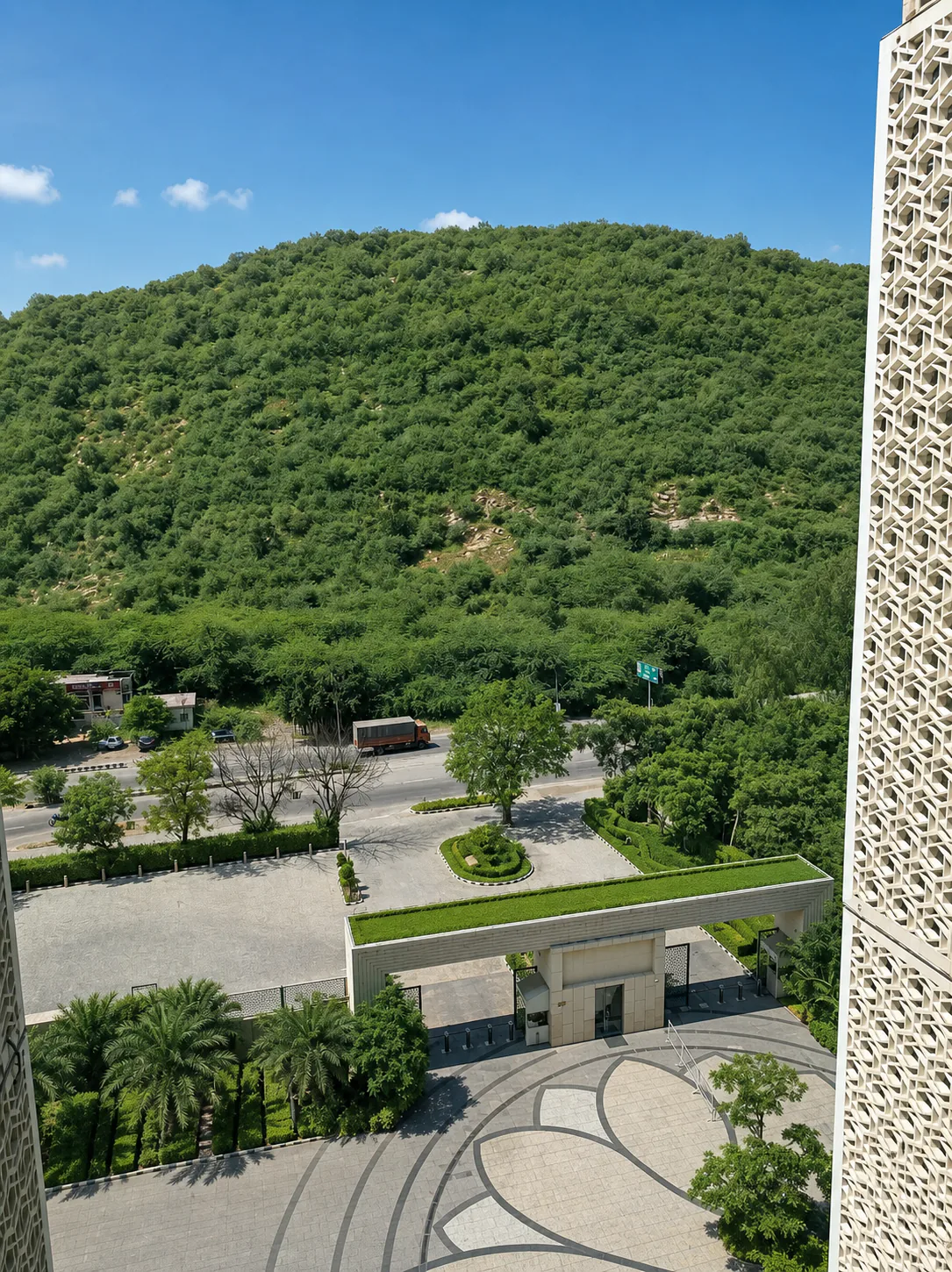 Elevated view of the Taj Amer Jaipur entrance court, palm grove and gate roof against the Aravalli hillside.