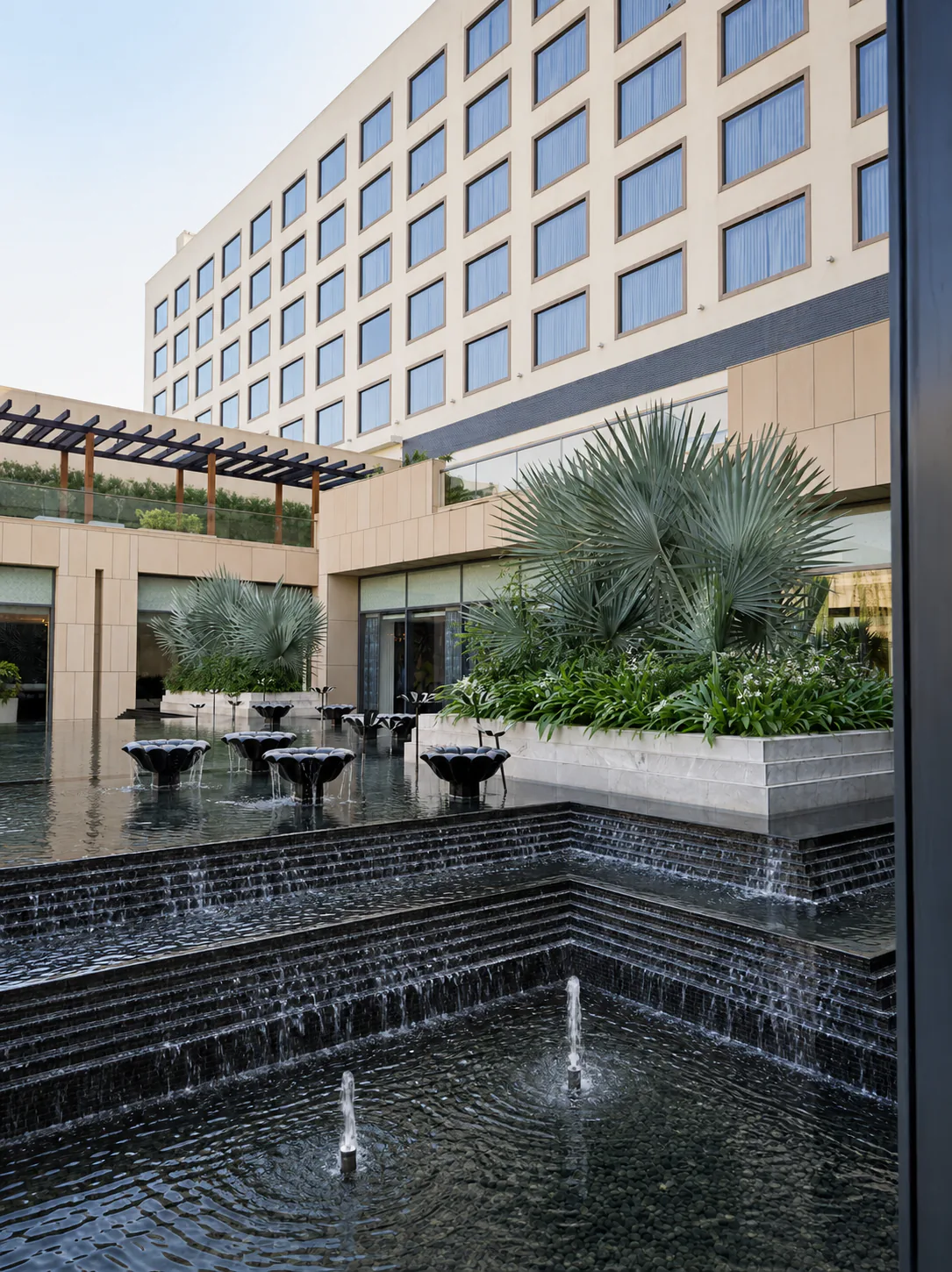 Taj Amer Jaipur courtyard with black stepped cascades, fountain jets and silver fan-palm planters.