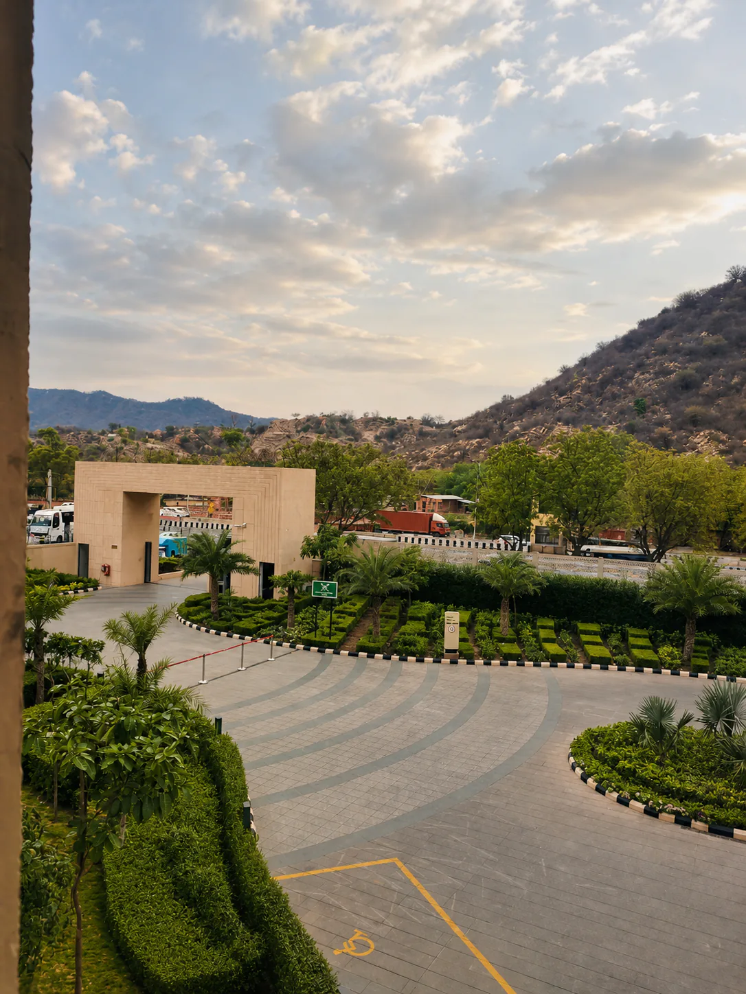 Taj Amer Jaipur formal entrance garden with geometric hedges, palms, curved paving and rocky hills.