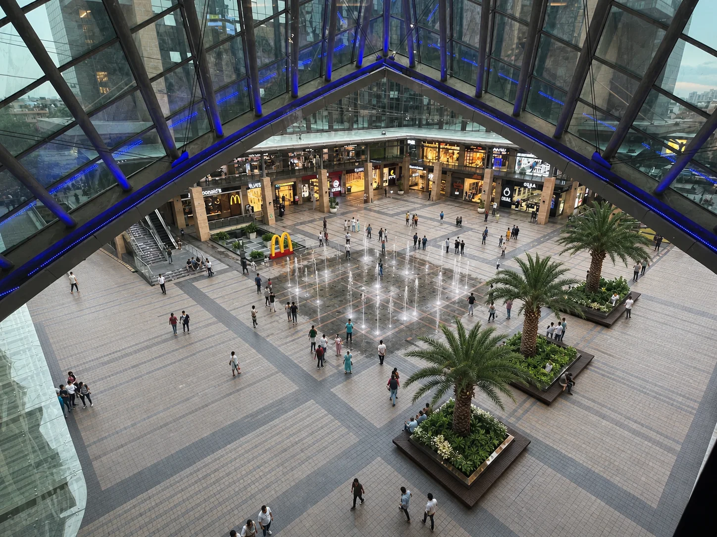 Elevated view of Vegas Mall Dwarka central court with fountain grid, palms, planted seating islands and pedestrian paving.