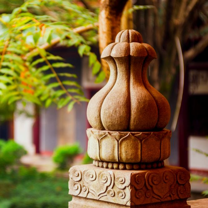 A detailed garden sculpture curated by Four Leaf Landscape, depicting a traditional stone carving with intricate patterns, set against a soft-focus background of a garden setting.