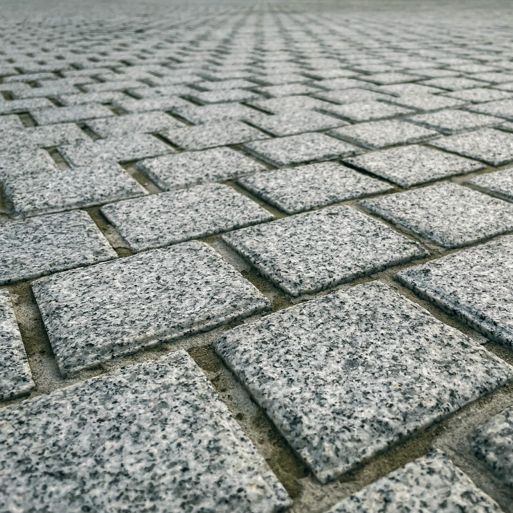 Close-up of a granite cobblestone pavement with a meticulous herringbone pattern installation by Four Leaf Landscape, highlighting precision in civil works and hardscape services.