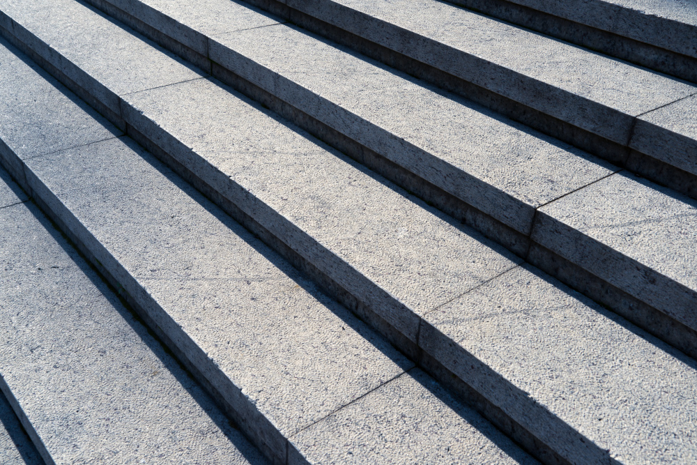 The clean, angular lines of concrete stair steps casting sharp shadows in the sunlight, showcasing Four Leaf Landscape's expertise in hardscape craftsmanship.