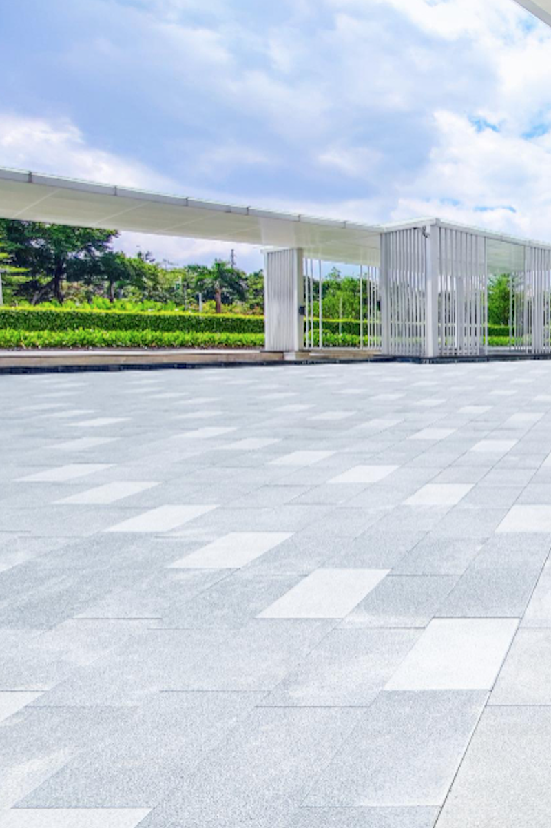 A contemporary hardscape featuring a patterned pavement with geometric tiles, framed by minimalist white structures and vibrant greenery, crafted by Four Leaf Landscape.