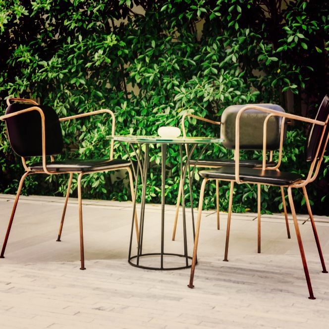 A tastefully arranged outdoor furniture set by Four Leaf Landscape featuring sleek metal chairs and a round table, set against a backdrop of lush foliage, epitomizing stylish outdoor living.